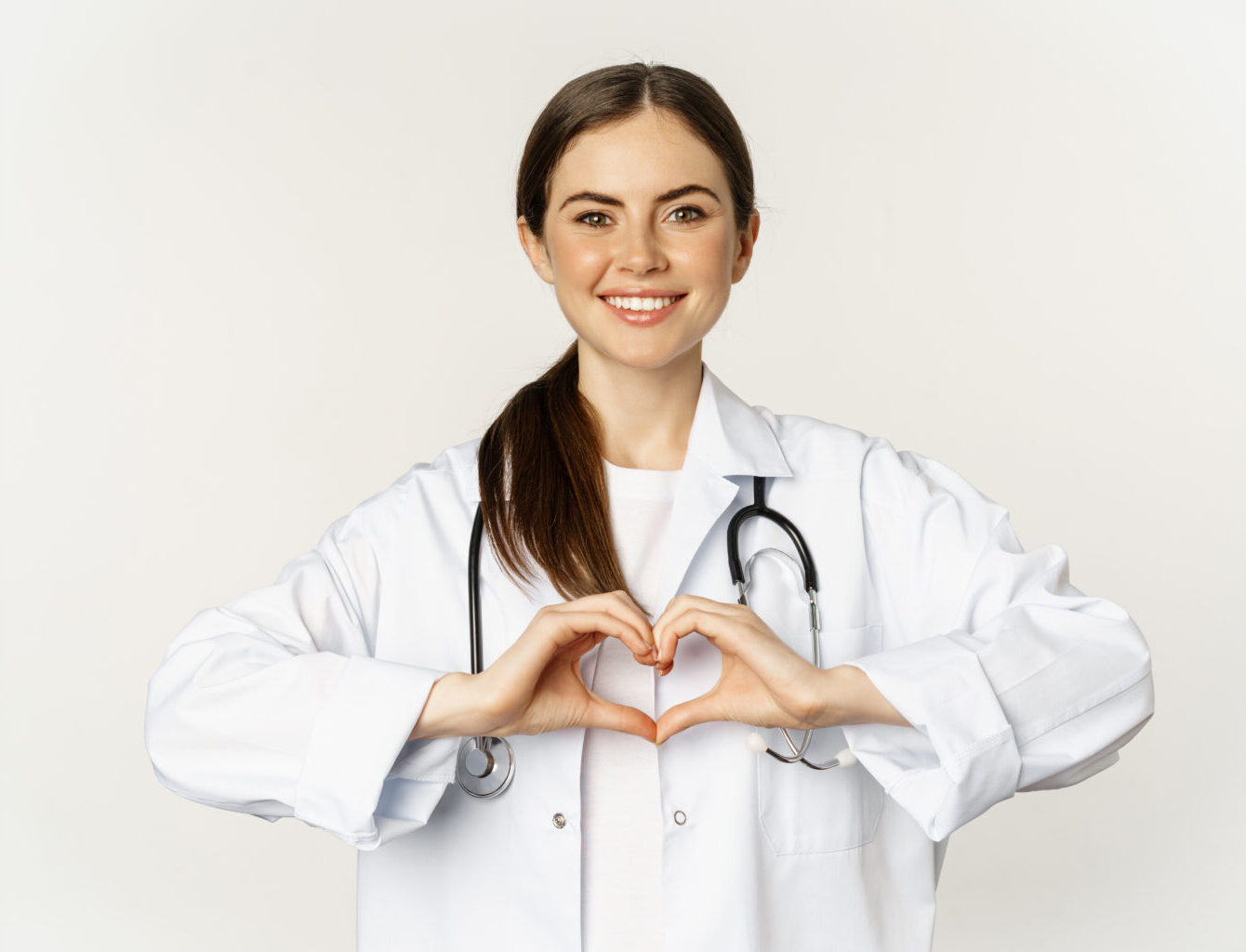 Portrait of smiling doctor, female physician showing heart sign and looking with care, love her patients, standing over white background